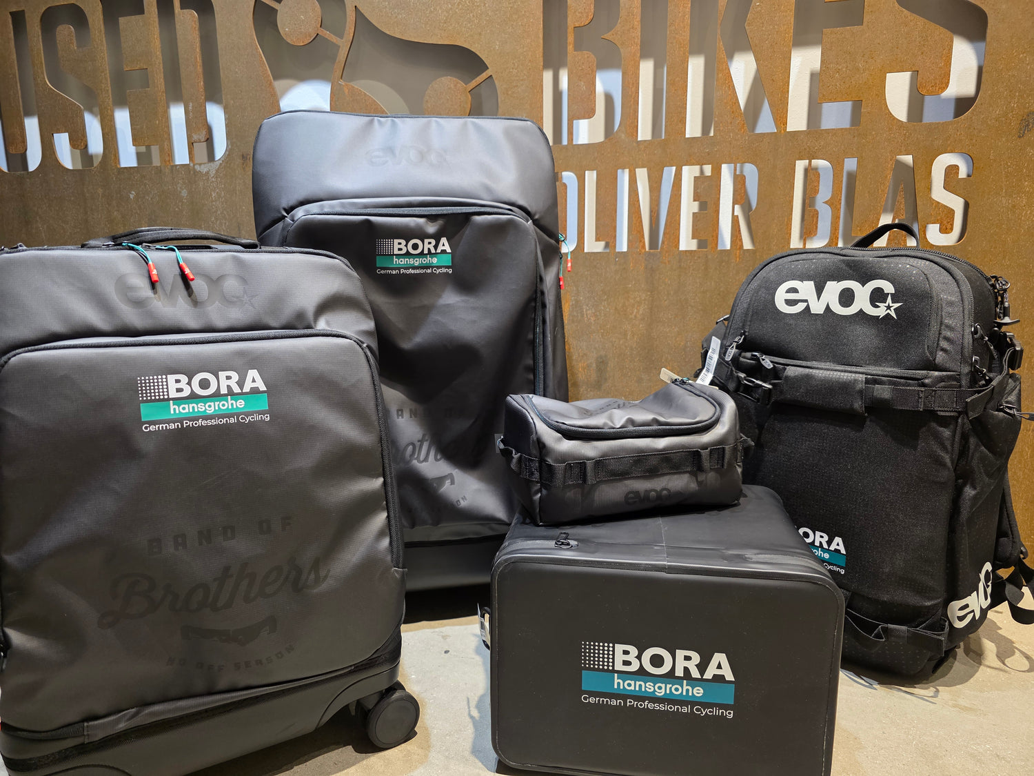 Taschen und Koffer der Firma EVOC im BORA-hansgrohe Teamdesign vor USEDBIKES-OB.DE Schild