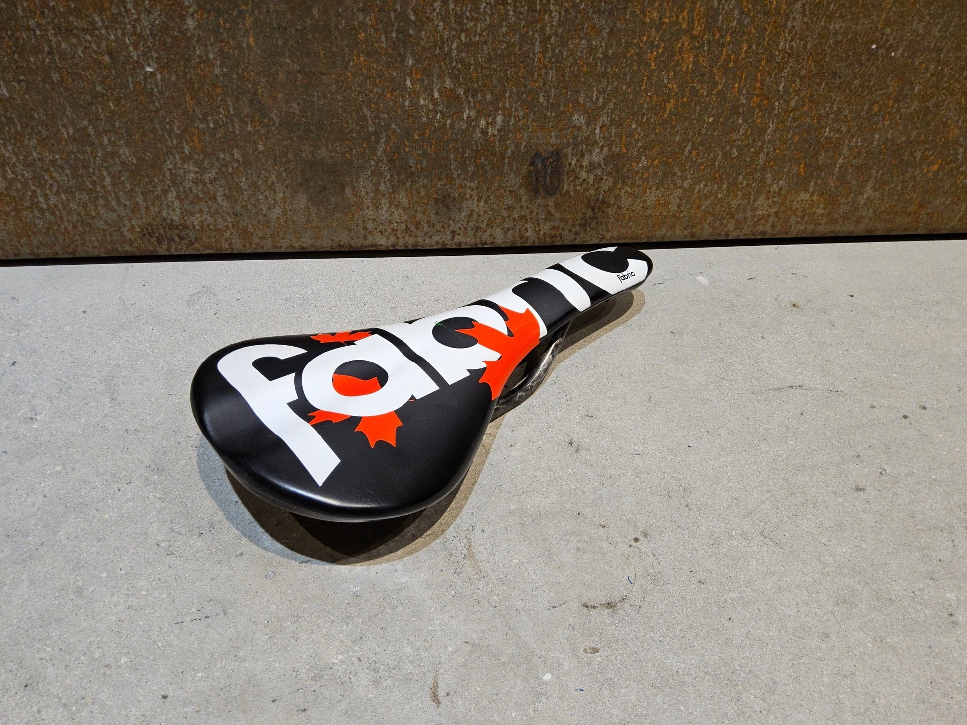 Sattel von Fabric, FABRIC SCOOP PRO TEAM FLAT SATTEL MAPLE LEAF / 142MM in variant_title vor USEDBIKES - OB.DE Hintergrund