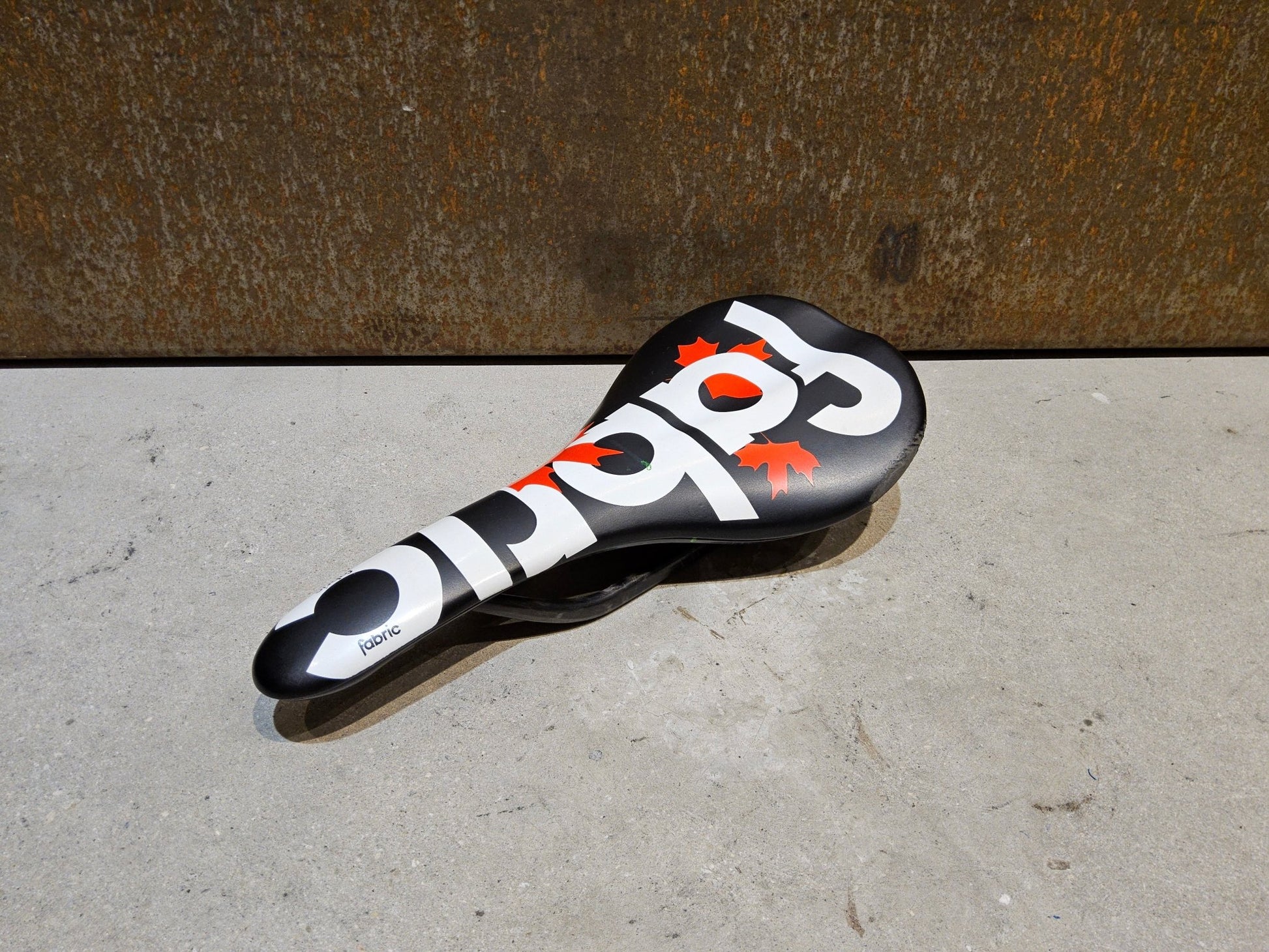 Sattel von Fabric, FABRIC SCOOP PRO TEAM FLAT SATTEL MAPLE LEAF / 142MM in variant_title vor USEDBIKES - OB.DE Hintergrund