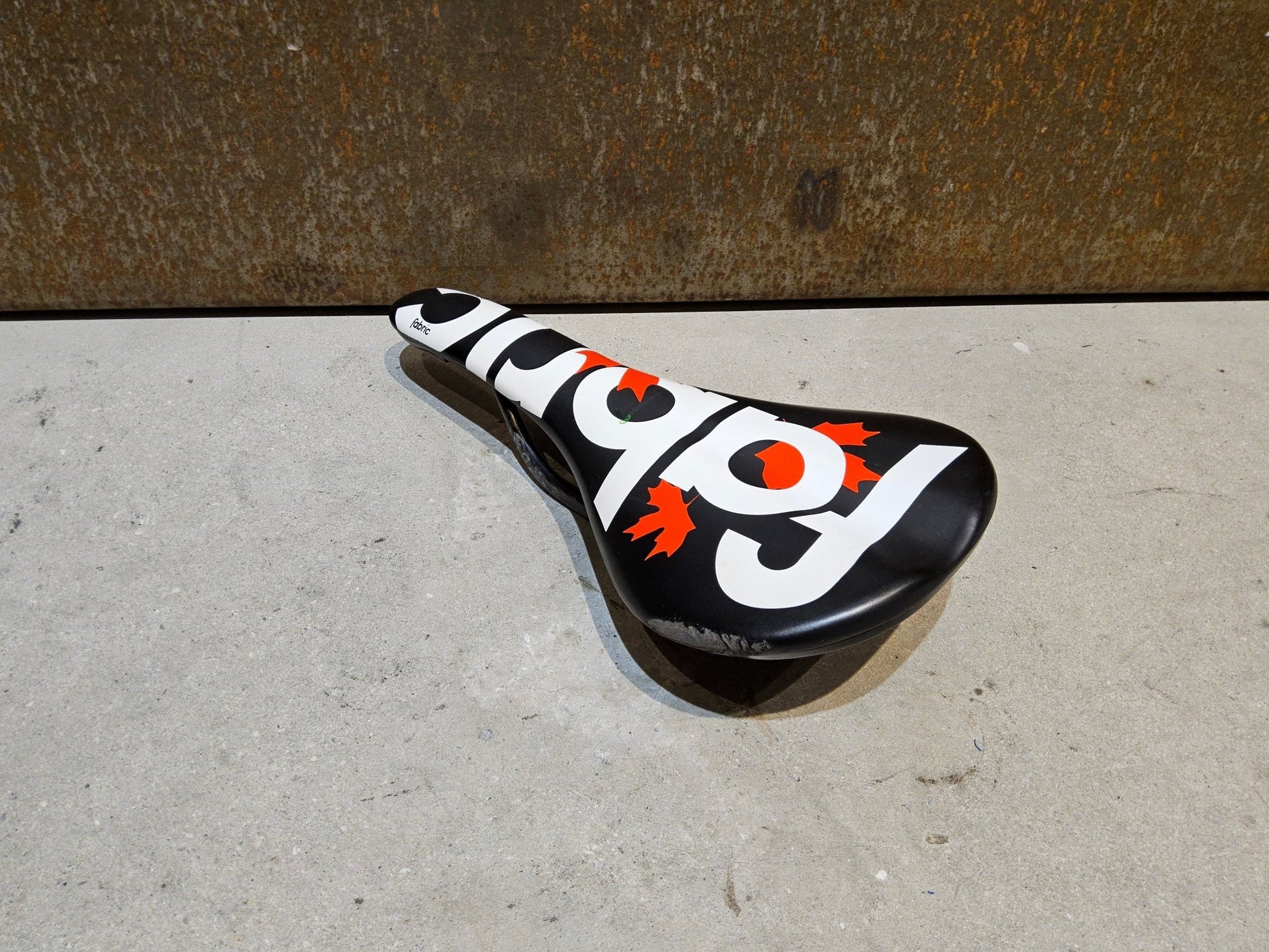 Sattel von Fabric, FABRIC SCOOP PRO TEAM FLAT SATTEL MAPLE LEAF / 142MM in variant_title vor USEDBIKES - OB.DE Hintergrund