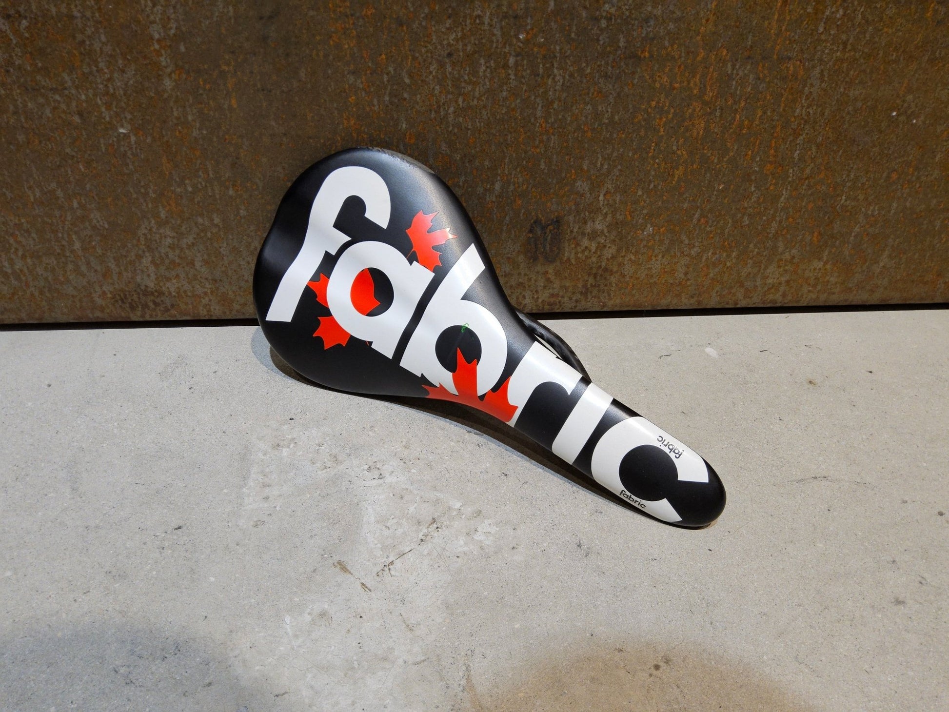 Sattel von Fabric, FABRIC SCOOP PRO TEAM FLAT SATTEL MAPLE LEAF / 142MM in variant_title vor USEDBIKES - OB.DE Hintergrund