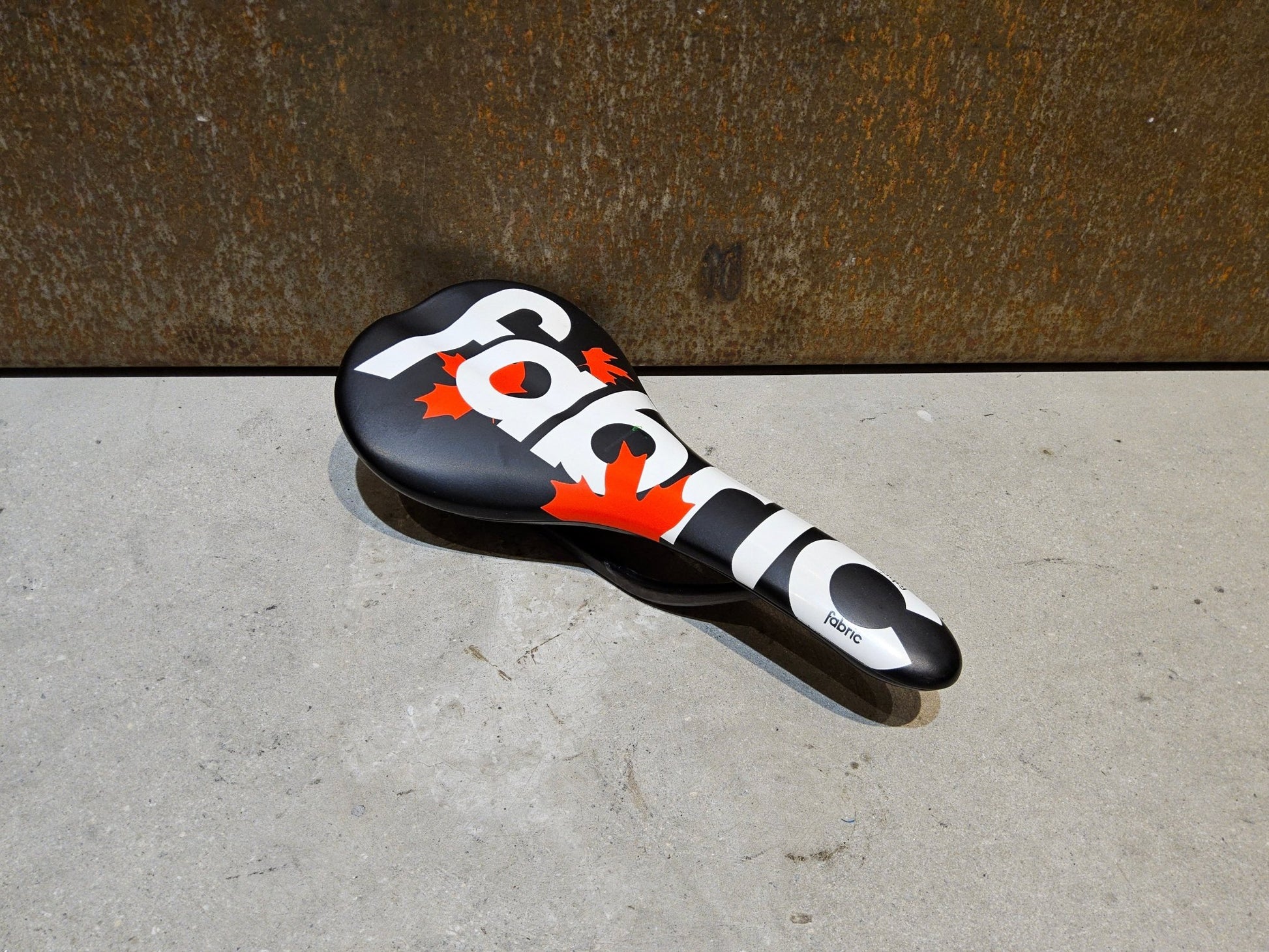 Sattel von Fabric, FABRIC SCOOP PRO TEAM FLAT SATTEL MAPLE LEAF / 142MM in variant_title vor USEDBIKES - OB.DE Hintergrund