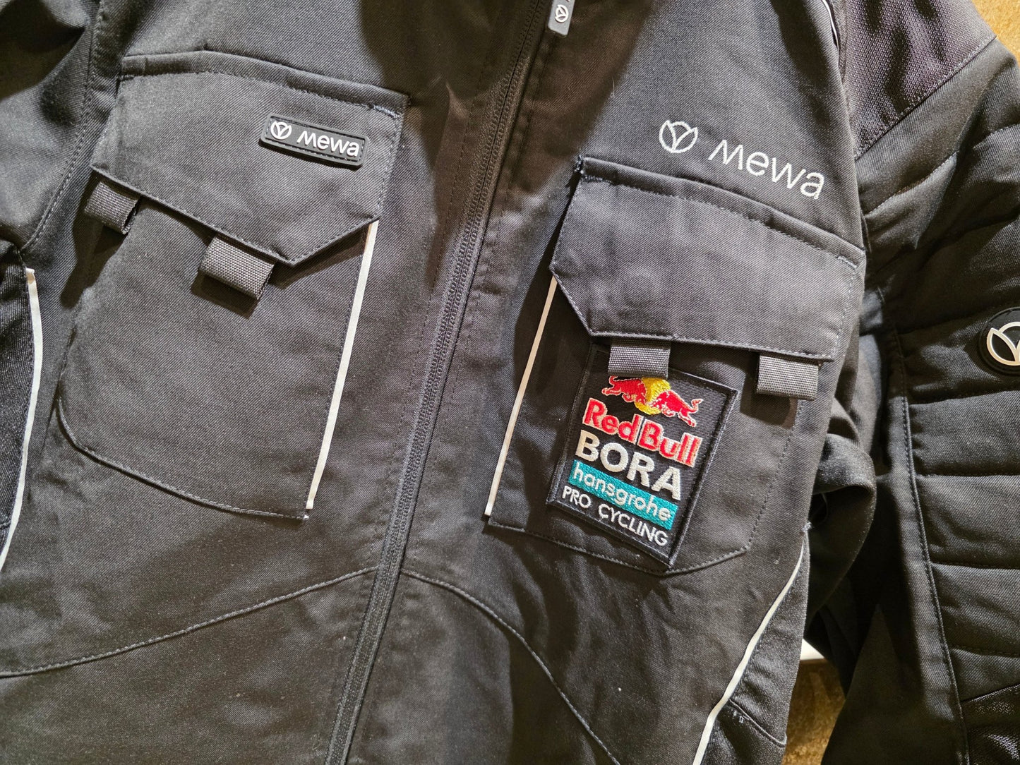 Freizeitbekleidung - BOH von Mewa, MEWA RED BULL - BORA HANSGROHE PEAK ARBEITSJACKE STAFF / HERREN in variant_title vor USEDBIKES - OB.DE Hintergrund