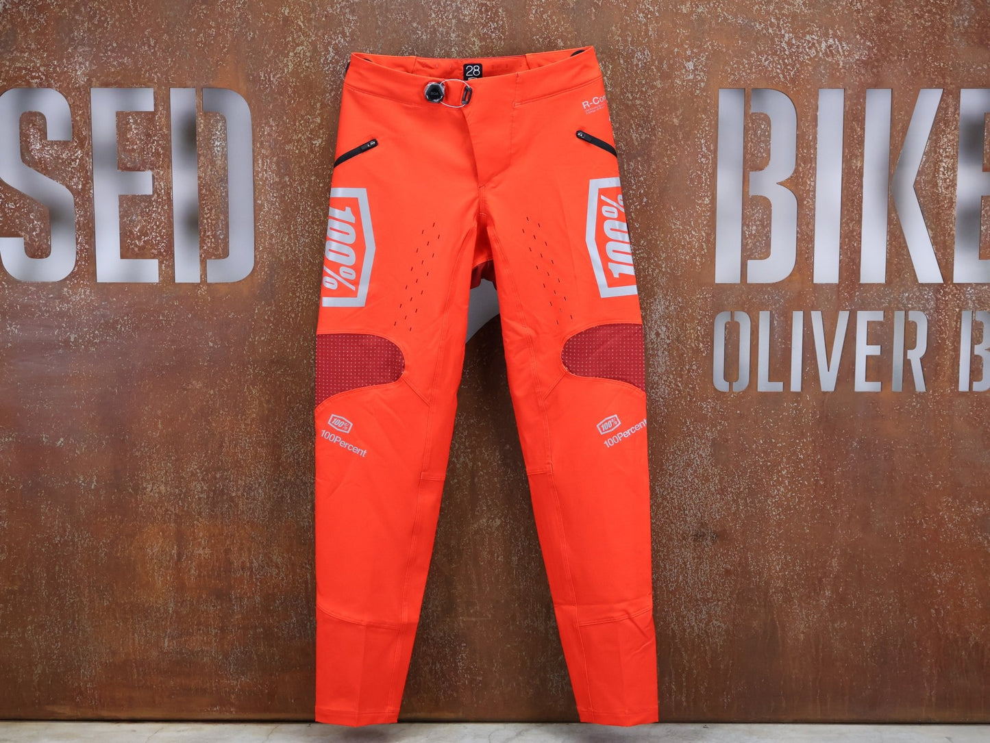 Hosen Herren von 100%, 100% – R - CORE X PANTS / ORANGE - RED / TREK FACTORY RACING TEAM / 4 - WAY STRETCH vor USEDBIKES - OB.DE Hintergrund