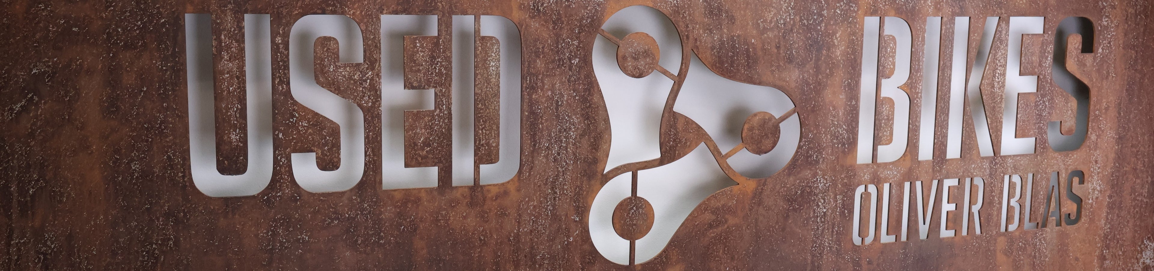 Verrostetes Stahlblech mit ausgeschnittener USED BIKES OLI ER BLAS Schrift auf weißem Hintergrund.