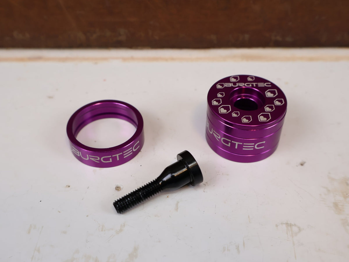 Vorbau von Burgtec, Burgtec Spacer Set Top Cap + Bolt Purple Rain Schwarz vor USEDBIKES-OB.DE Hintergrund