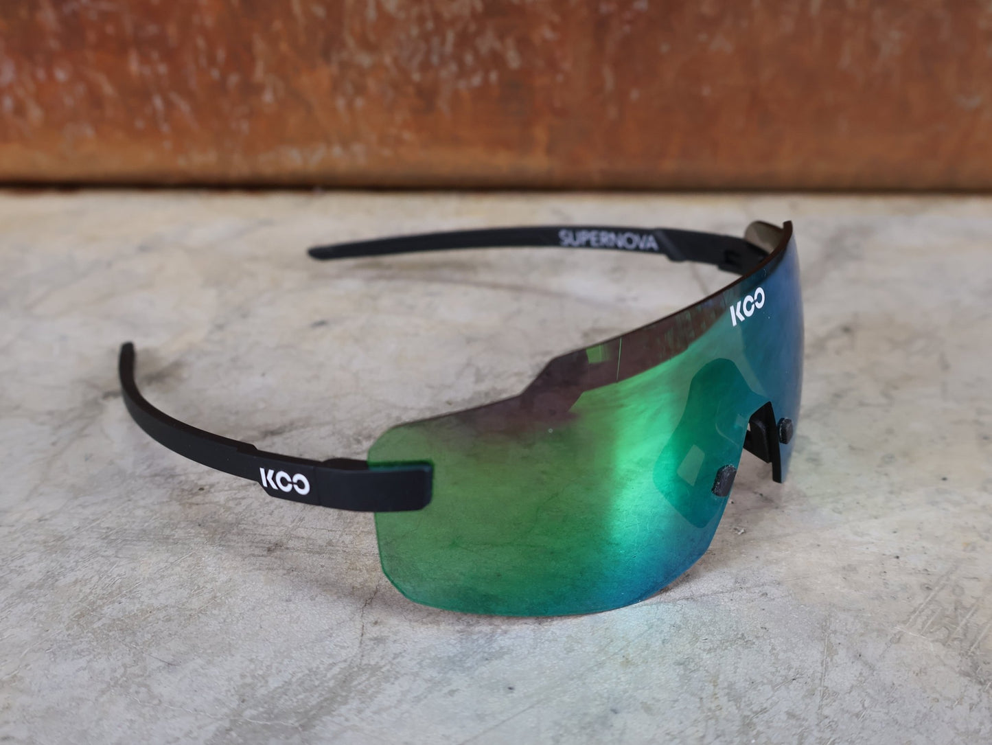 Brillen von Koo, KOO SUPERNOVA SONNENBRILLE / BLACK MATT GREEN MIRROR vor USEDBIKES - OB.DE Hintergrund