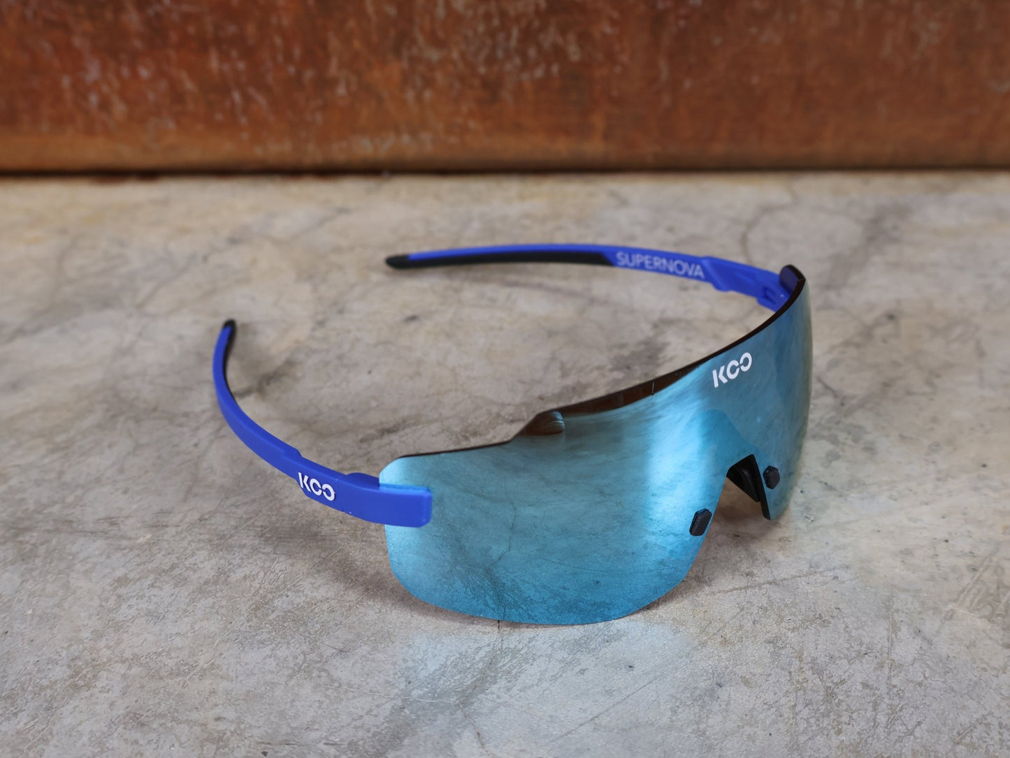 Brillen von Koo, KOO SUPERNOVA SONNENBRILLE / BLUE MATT TURQUOISE MIRROR vor USEDBIKES - OB.DE Hintergrund