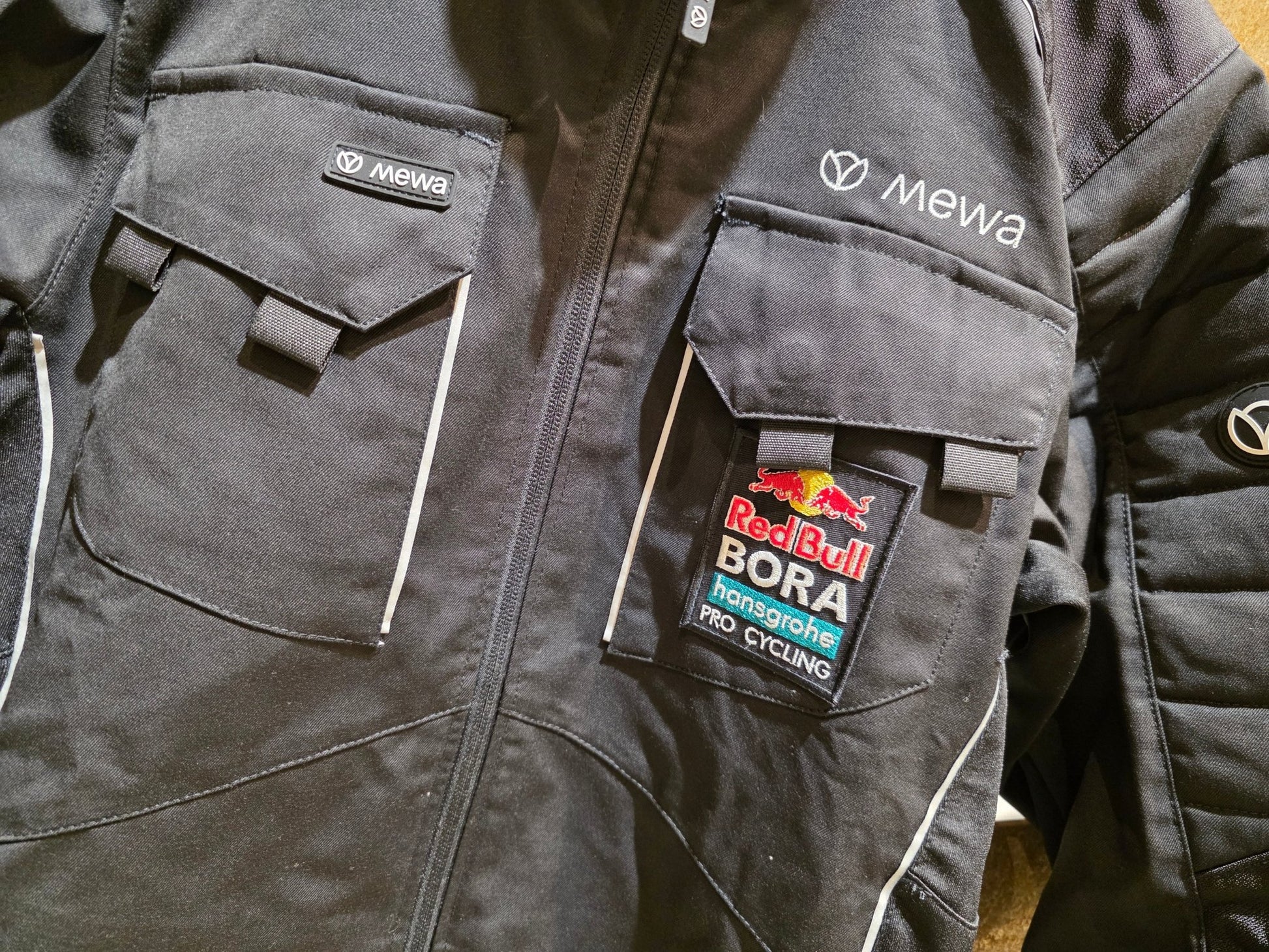 Freizeitbekleidung - BOH von Mewa, MEWA RED BULL - BORA HANSGROHE PEAK ARBEITSJACKE STAFF / HERREN in variant_title vor USEDBIKES - OB.DE Hintergrund