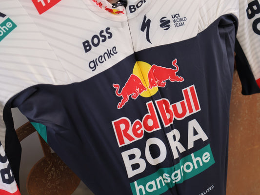 Anzug - BOH von Specialized, Red Bull BORA hansgrohe Aero Skinsuit Kurzarm Specialized vor USEDBIKES-OB.DE Hintergrund