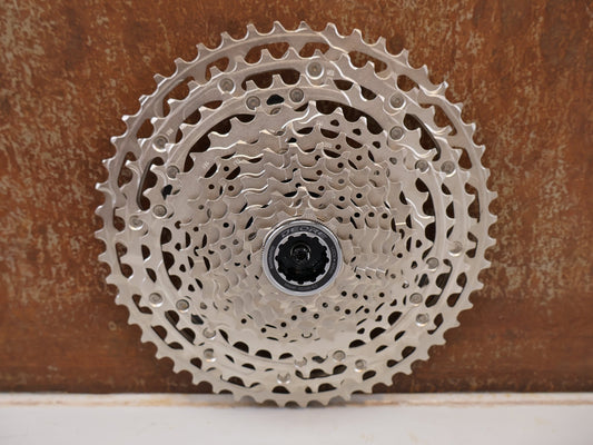 Kassette & Zahnkränze von Shimano, SHIMANO DEORE CS-M5100 KASSETTE / 11-FACH 11-51 ZÄHNE HG RITZELPAKET vor USEDBIKES-OB.DE Hintergrund