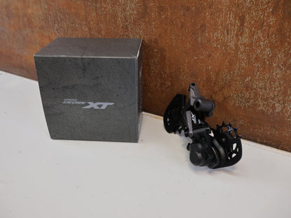 Schaltungsteile von Shimano, SHIMANO DEORE XT RD-M8120 / SCHALTWERK / 2X12-FACH / LONG CAGE vor USEDBIKES-OB.DE Hintergrund