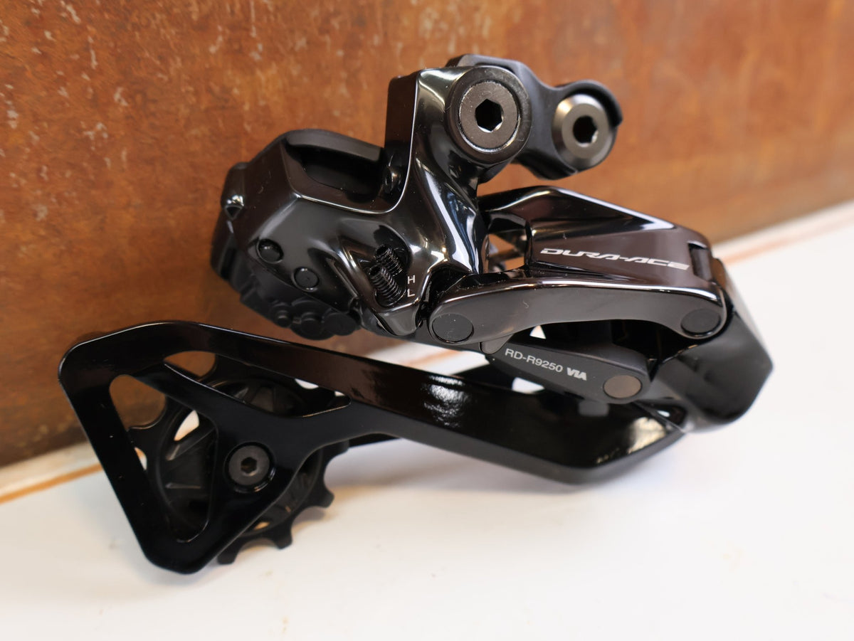 Schaltungsteile von Shimano, Shimano Dura-Ace Di2 RD-R9250 12-fach Schaltwerk Carbon vor USEDBIKES-OB.DE Hintergrund