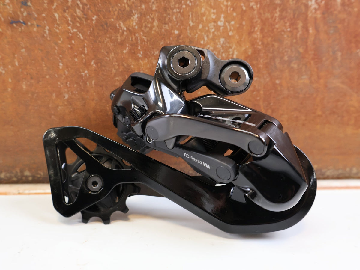 Schaltungsteile von Shimano, Shimano Dura-Ace Di2 RD-R9250 12-fach Schaltwerk Carbon vor USEDBIKES-OB.DE Hintergrund