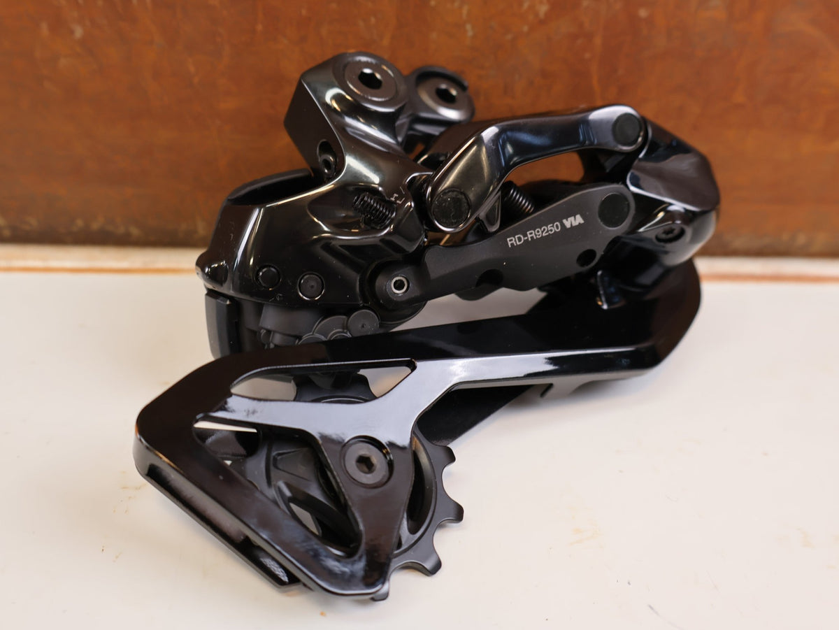 Schaltungsteile von Shimano, Shimano Dura-Ace Di2 RD-R9250 12-fach Schaltwerk Carbon vor USEDBIKES-OB.DE Hintergrund