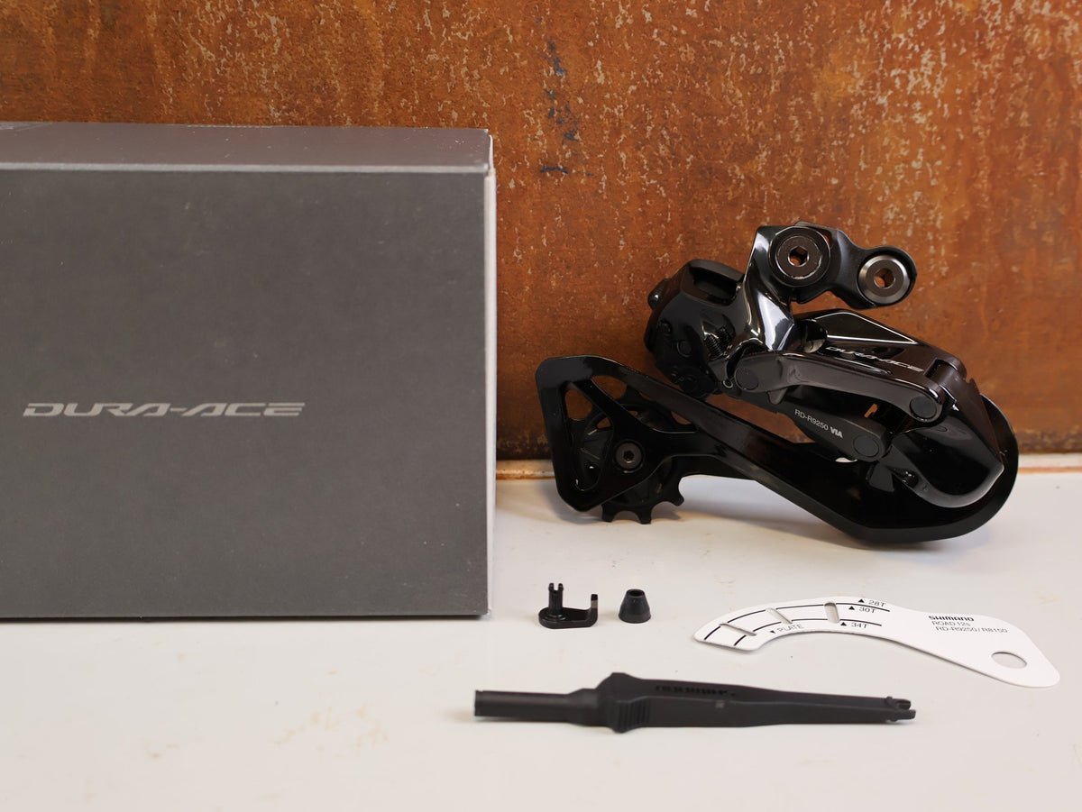 Schaltungsteile von Shimano, Shimano Dura-Ace Di2 RD-R9250 12-fach Schaltwerk Carbon vor USEDBIKES-OB.DE Hintergrund