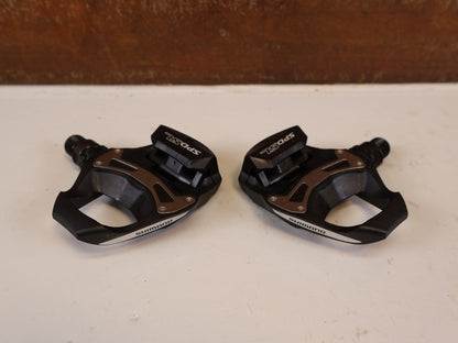 Pedale von Shimano, SHIMANO PD R550 COMPOSITE SPD SL RENNRAD PEDALE vor USEDBIKES-OB.DE Hintergrund