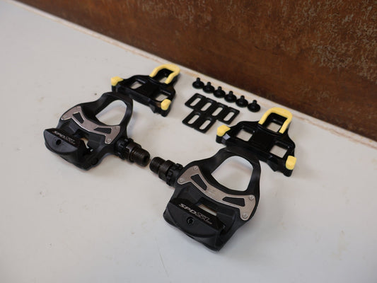 Pedale von Shimano, SHIMANO PD-R550 SPD-SL PEDALE / KLICKPEDAL ROAD RENNRAD SCHWARZ INKL CLEATS vor USEDBIKES-OB.DE Hintergrund