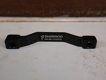 Zubehör von Shimano, SHIMANO POSTMOUNT ADAPTER PM 203 AUF 220 MM SM-MA-F220P/PL vor USEDBIKES-OB.DE Hintergrund