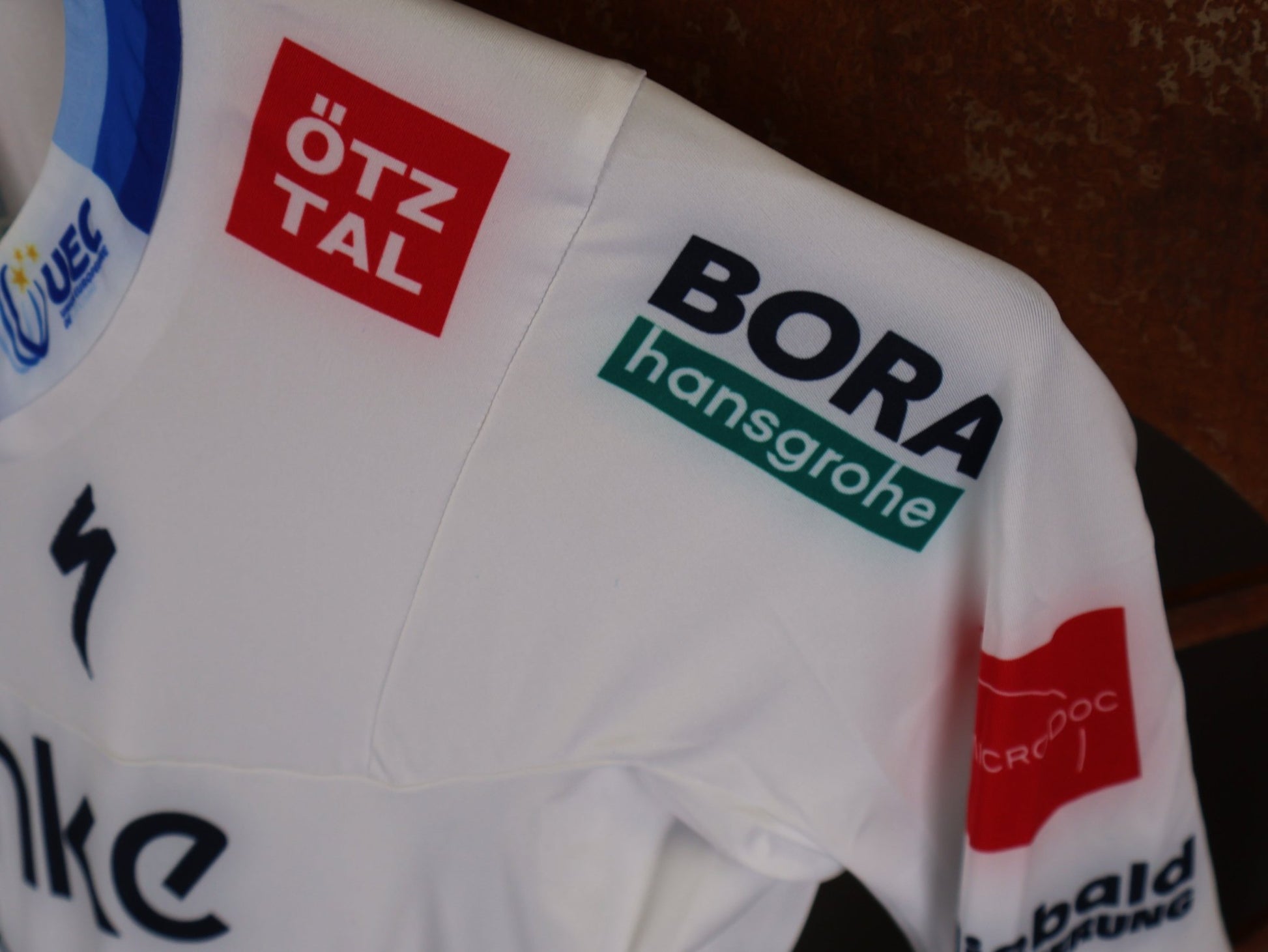 Anzug - BOH von Specialized, SPECIALIZED TGA ROOKIES OF RED BULL - BORA HANSGROHE AERO SKIN SUIT LS / EUROPEAN CHAMPION vor USEDBIKES - OB.DE Hintergrund