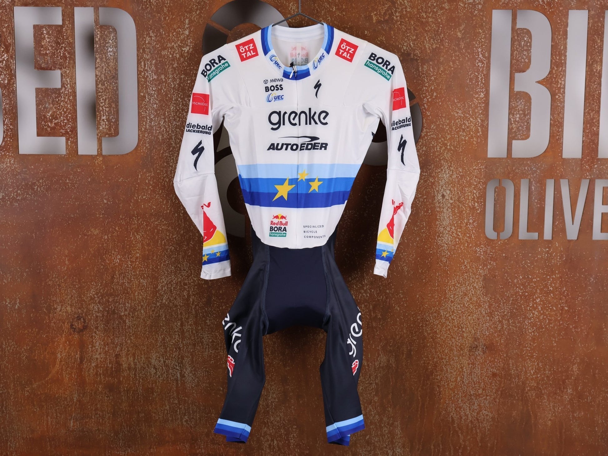 Anzug - BOH von Specialized, SPECIALIZED TGA ROOKIES OF RED BULL - BORA HANSGROHE AERO SKIN SUIT LS / EUROPEAN CHAMPION vor USEDBIKES - OB.DE Hintergrund