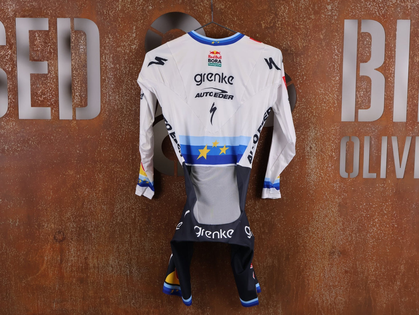 Anzug - BOH von Specialized, SPECIALIZED TGA ROOKIES OF RED BULL - BORA HANSGROHE AERO SKIN SUIT LS / EUROPEAN CHAMPION vor USEDBIKES - OB.DE Hintergrund