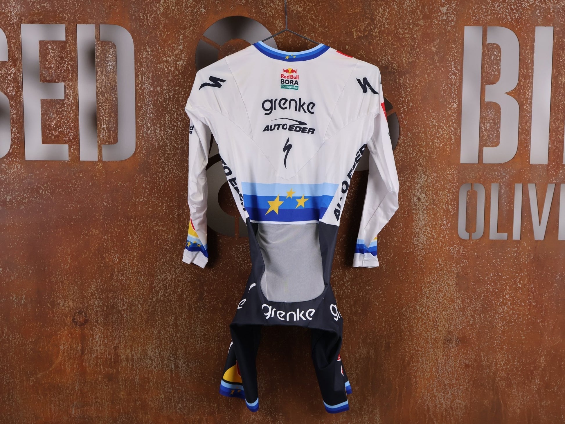 Anzug - BOH von Specialized, SPECIALIZED TGA ROOKIES OF RED BULL - BORA HANSGROHE AERO SKIN SUIT LS / EUROPEAN CHAMPION vor USEDBIKES - OB.DE Hintergrund