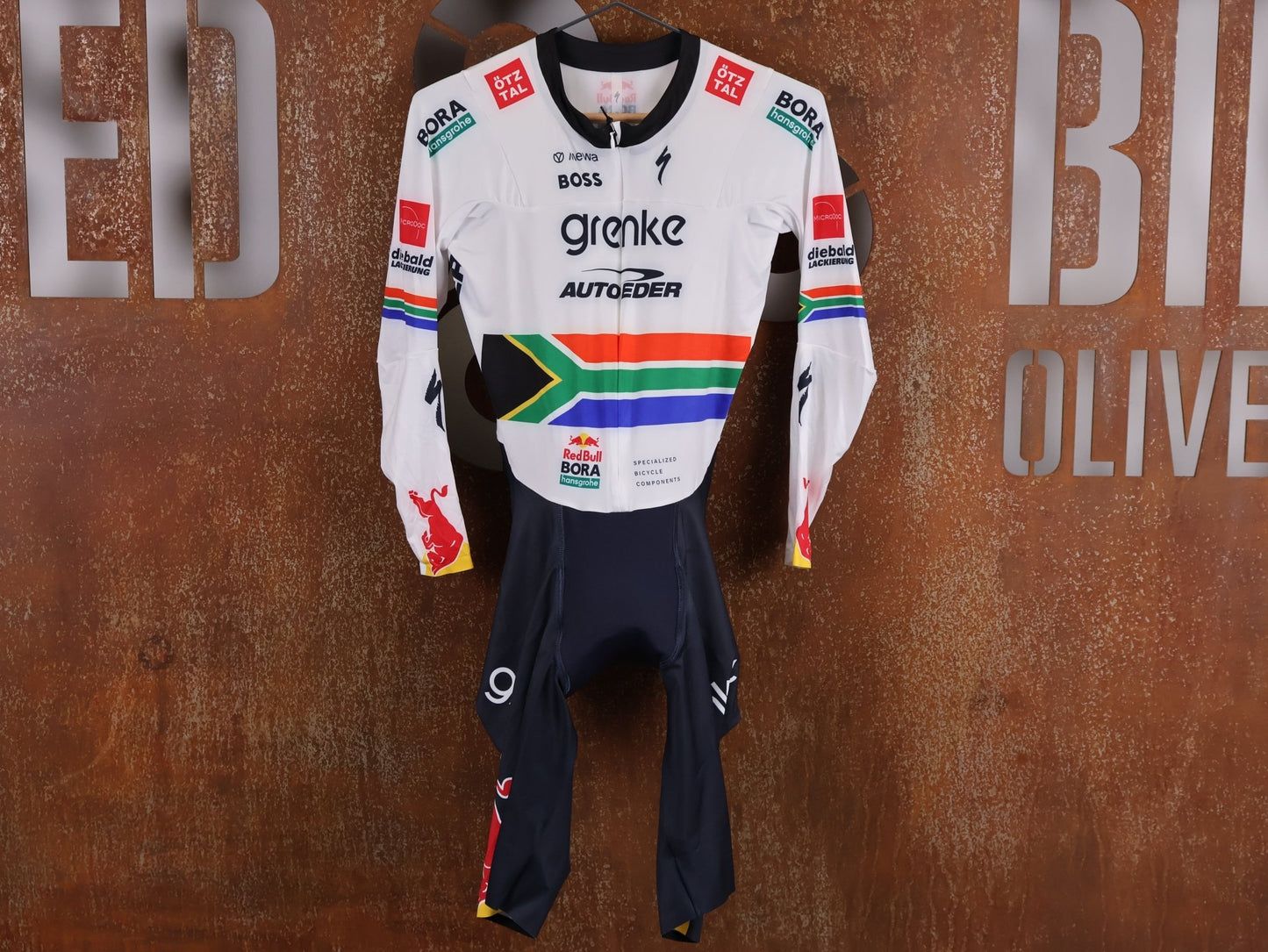 Anzug - BOH von Specialized, SPECIALIZED TGA ROOKIES OF RED BULL - BORA HANSGROHE AERO SKIN SUIT LS / SOUTH AFRICA CHAMPION vor USEDBIKES - OB.DE Hintergrund