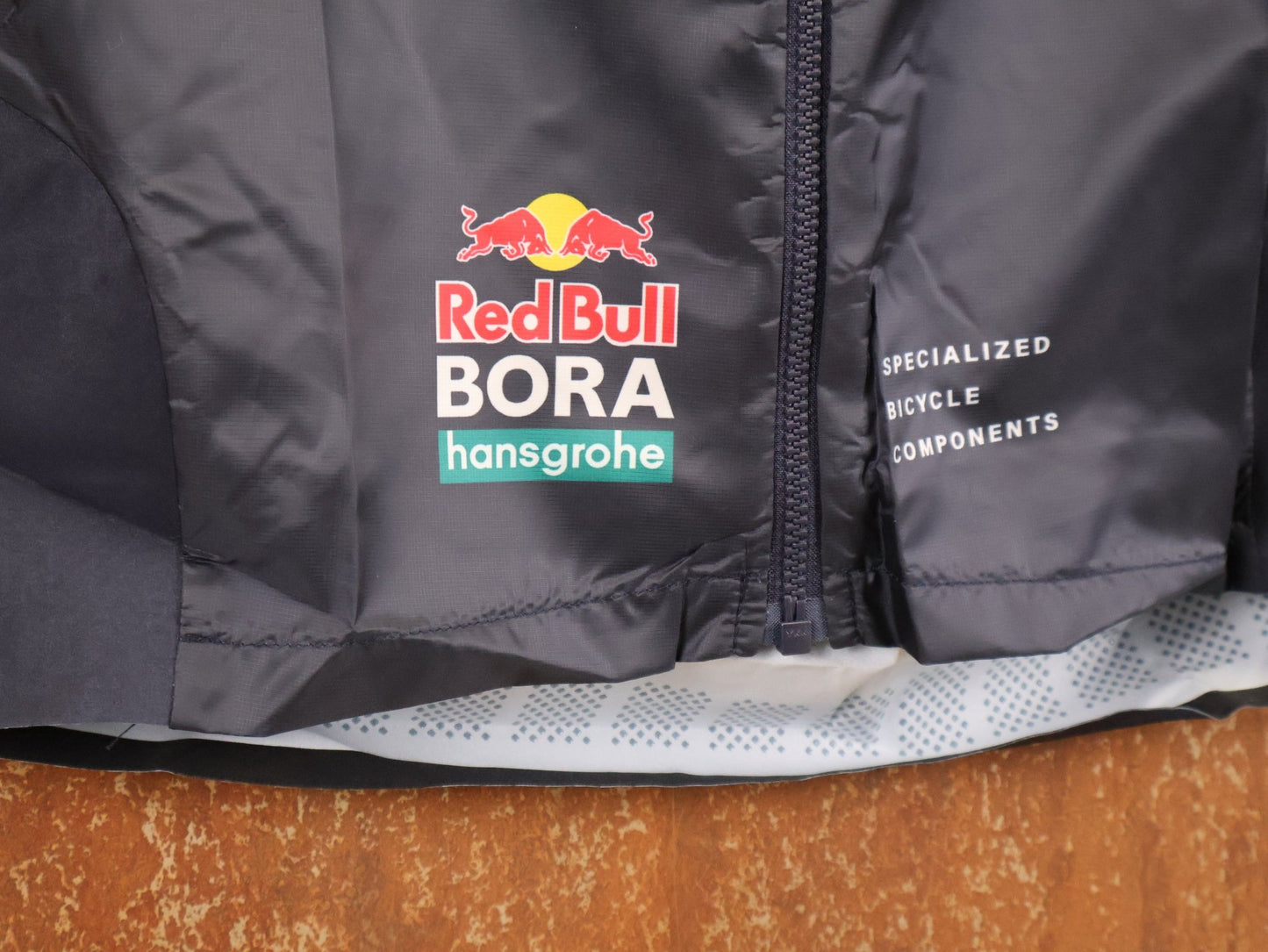 Westen - BOH von Specialized, SPECIALIZED TGA ROOKIES OF RED BULL - BORA HANSGROHE WIND VEST / WESTE vor USEDBIKES - OB.DE Hintergrund