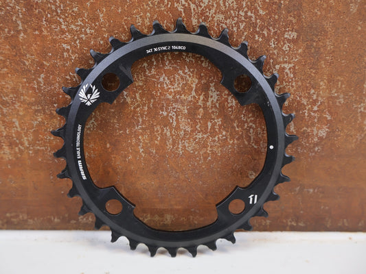 Kettenblatt von Sram, SRAM X-SYNC 2 EAGLE KETTENBLATT 34T 104 MM BCD vor USEDBIKES-OB.DE Hintergrund