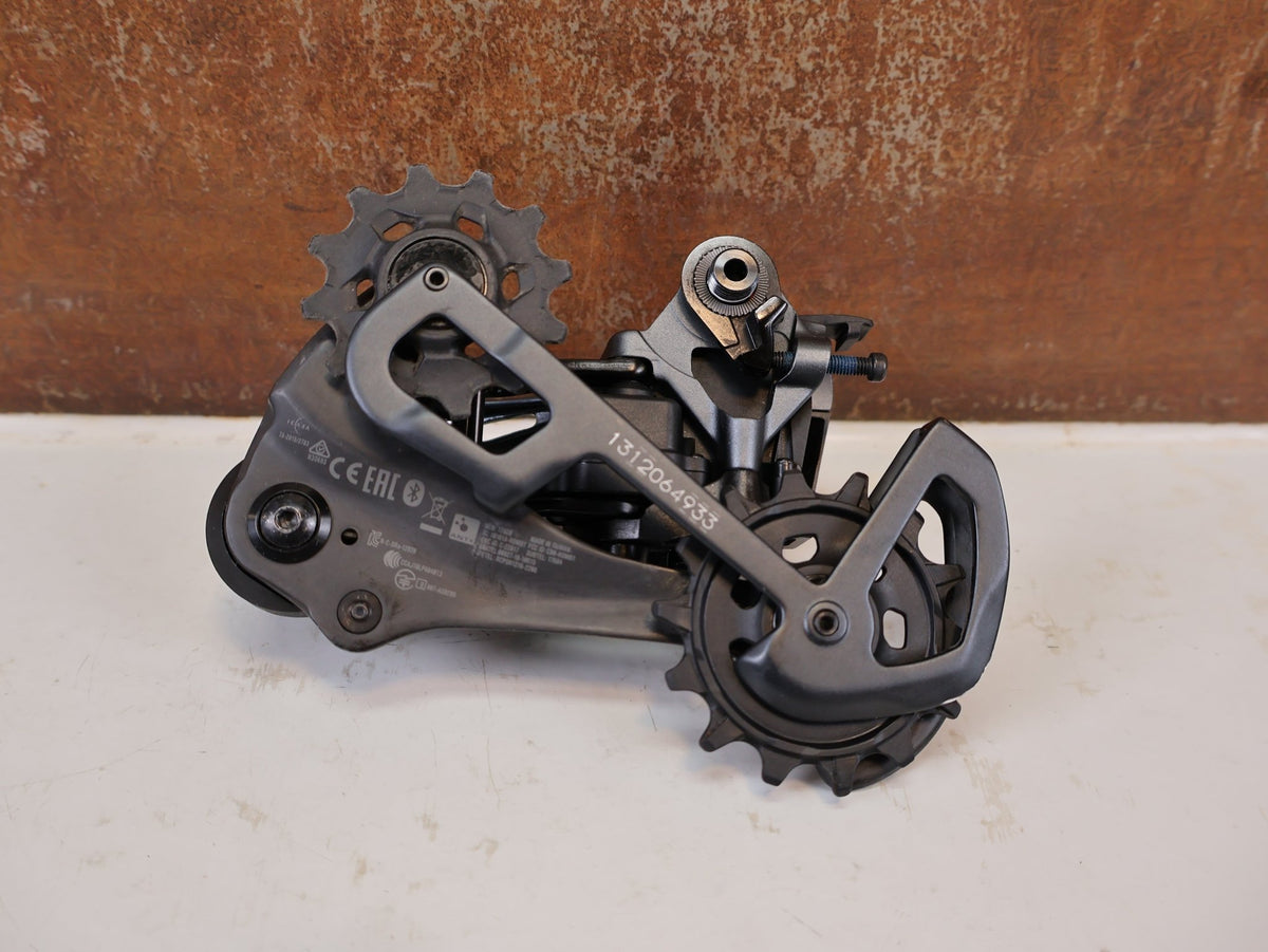Schaltungsteile von Sram, SRAM XX1 Eagle AXS 12-fach Schaltwerk 52Z Carbon Titan vor USEDBIKES-OB.DE Hintergrund