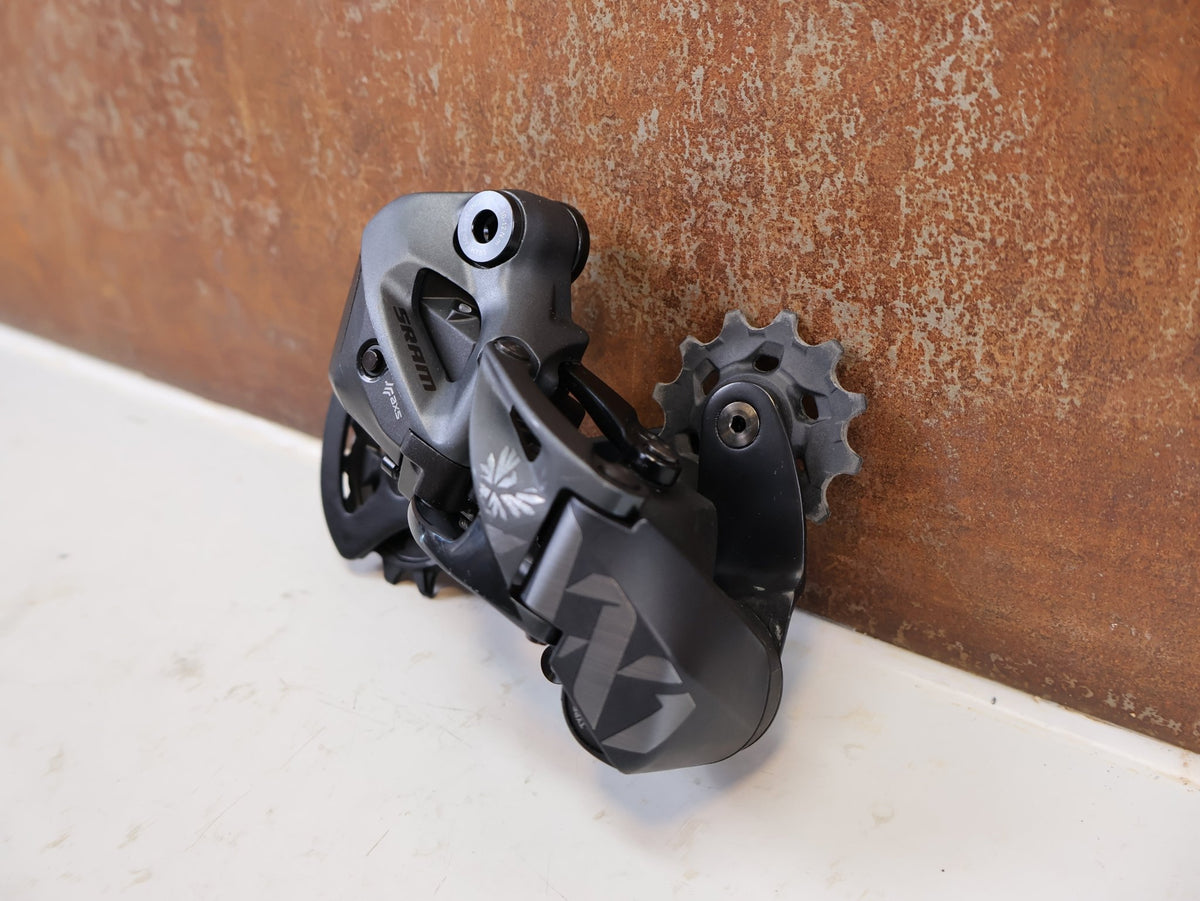 Schaltungsteile von Sram, SRAM XX1 Eagle AXS 12-fach Schaltwerk 52Z Carbon Titan vor USEDBIKES-OB.DE Hintergrund