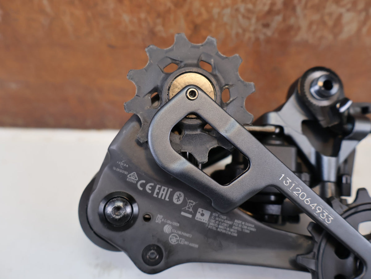 Schaltungsteile von Sram, SRAM XX1 Eagle AXS 12-fach Schaltwerk 52Z Carbon Titan vor USEDBIKES-OB.DE Hintergrund