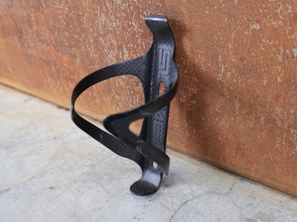 Trinkflaschen und Halter von Supacaz, SUPACAZ BLACK CARBON FLY FLASCHENHALTER / CARBON / 21 G vor USEDBIKES - OB.DE Hintergrund