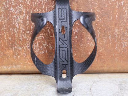 Trinkflaschen und Halter von Supacaz, SUPACAZ BLACK CARBON FLY FLASCHENHALTER / CARBON / 21 G vor USEDBIKES - OB.DE Hintergrund