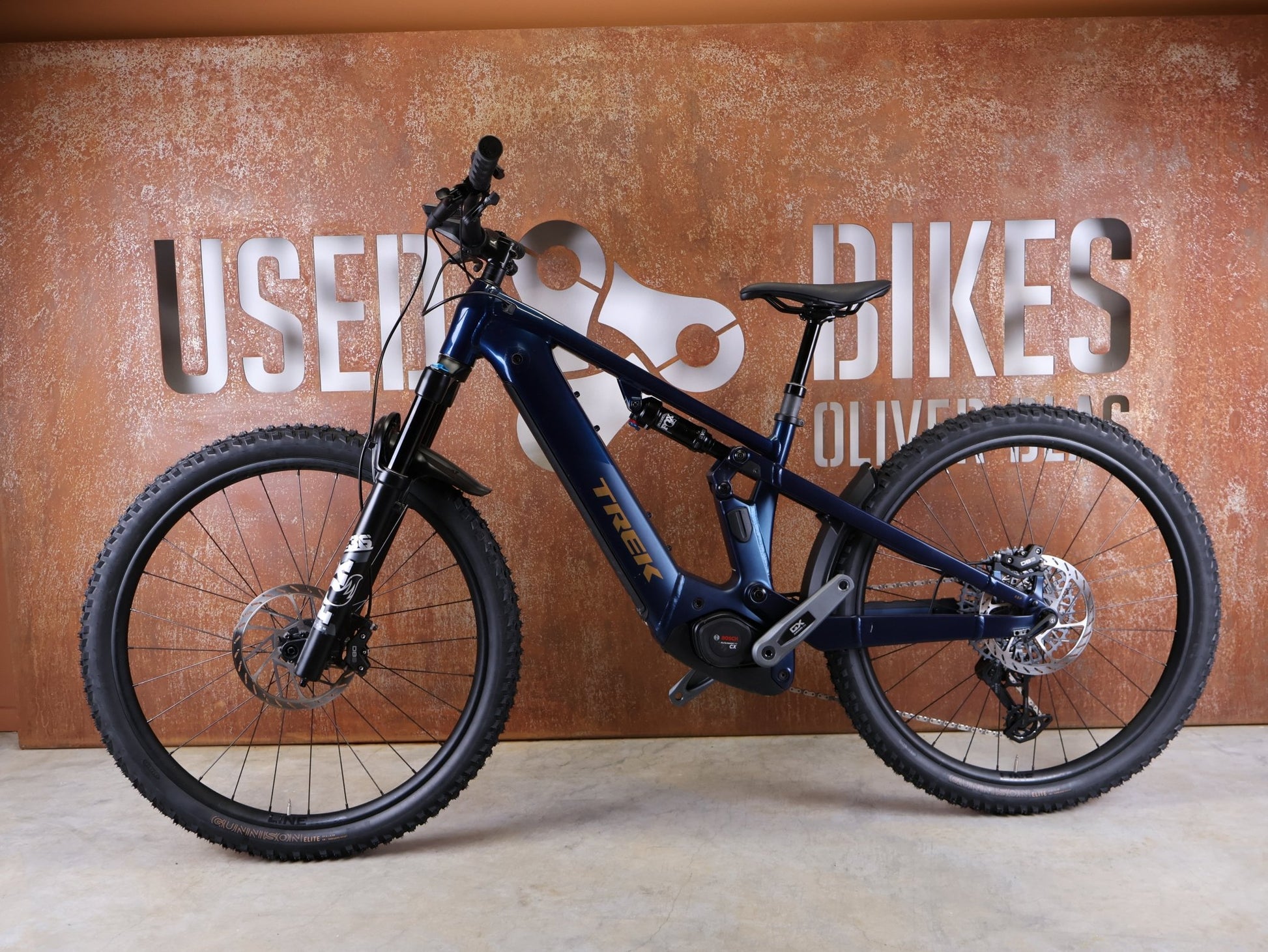 E - Mountainbike von Trek, TREK POWERFLY+ FS 8 GEN 4 / MATTE/GLOSS MULSANNE BLUE / S vor USEDBIKES - OB.DE Hintergrund